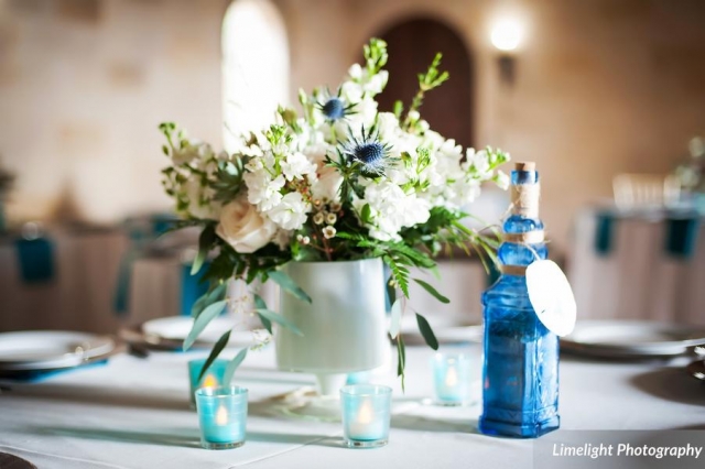 Beach themed wedding centerpiece of white and blue with thistle, roses, stock and wax flower.