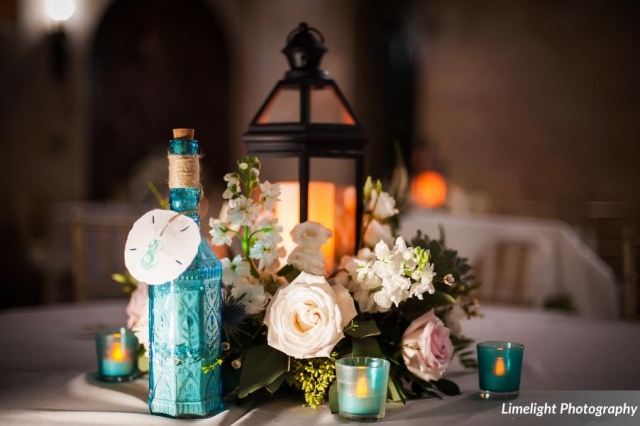 Beach themed wedding centerpiece with lantern and fresh flowers of white and blush with roses, lisianthus and stock.