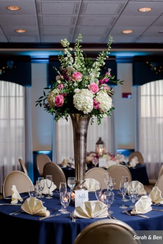 Elevated tall centerpiece in pink and white with hydrangeas, roses, delphinium and greenery.
