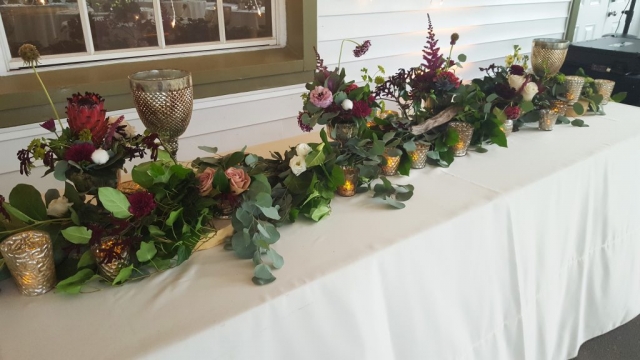Bohemian feast table with garland, candles and centerpieces in burgundy, raspberry and pink.