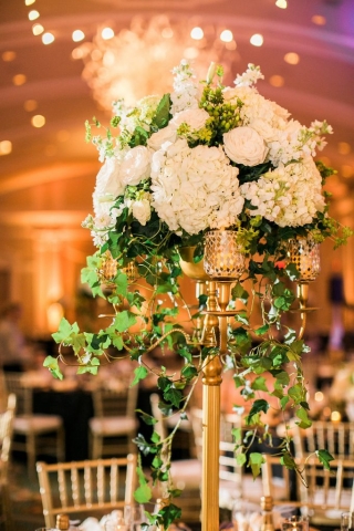 Elevated tall formal centerpiece in gold candelabra of all white hydrangeas, roses, stock and ivy.