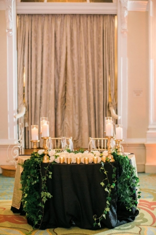 Elegant sweetheart table in gold with greenery and candles.
