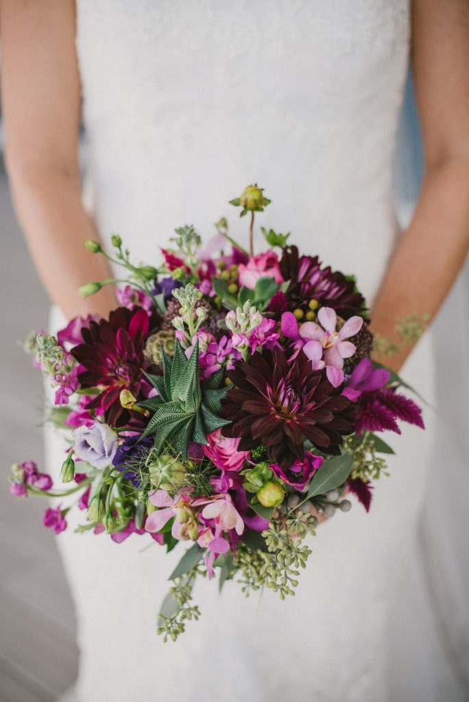 Textured bridal bouquet in burgundy and pinks with dahlias, succulents, orchids, celosia, ranunculus, nigella pods, scabiosa pods and eucalyptus.