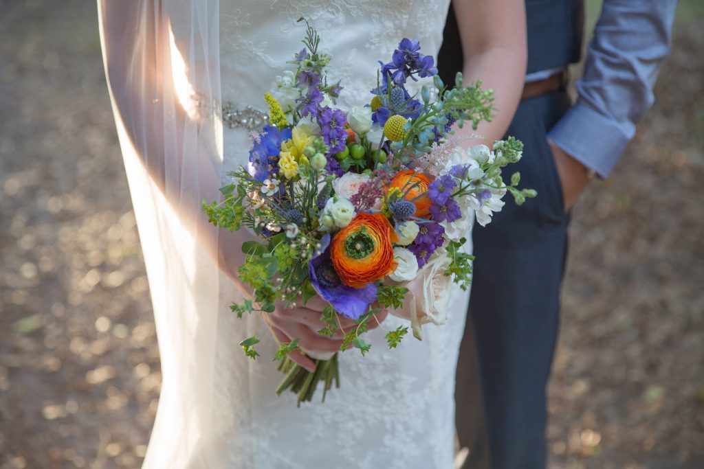 Bright wildflower bridal bouquet with ranunculus, larkspur, thistle, bille balls, delphinium, wax flower and roses.