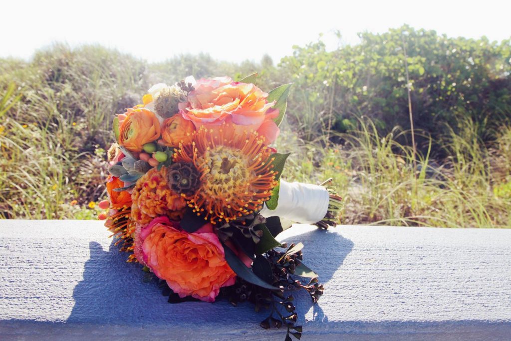 Autumn textured bridal bouquet in orange and brown with ranunculus, proteas, roses, scabiosa pods and eucalyptus.