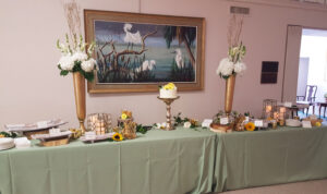 Buffet table decorated with elevated centerpiece, sunflowers and lanterns for anniversary party.
