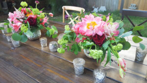 Two colorful peony centerpieces with silver votives on table for birthday party.