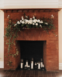 Organic style white flower arrangement on fireplace mantle and candles in fireplace at wedding reception at Orlo House in Tampa, Florida.