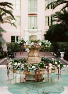 Fountain decorated with red hanging amaranthus, greenery and roses for wedding ceremony in the Vinoy Tea Garden in St. Petersburg, Florida.