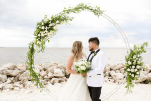 Classic moon gate with white flowers and greenery for beach ceremony in Tampa, Florida.