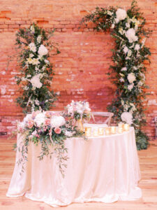 Garden style asymmetrical open arch sweetheart table backdrop with table arrangement at wedding reception at Armature Works in Tampa, Florida.