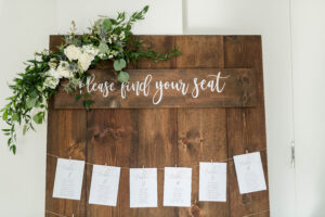 White flower and greenery corner piece on table seating chart for wedding reception.