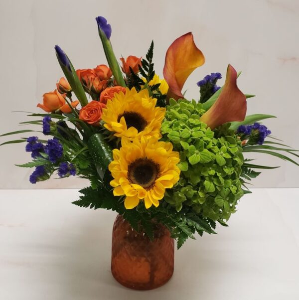 Bright yellow, orange, purple, and green flowers arranged in an orange textured container.