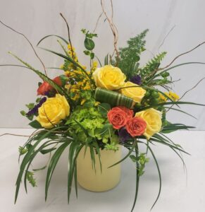 An organic arrangement of citrus colored flowers with robellini palm and curl willow in a yellow cylinder container