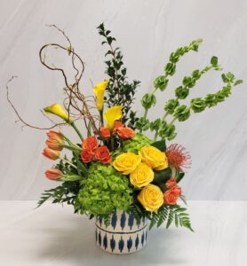 A bold and modern arrangement of yellow, orange, and green blooms in a keepsake blue and white ceramic container